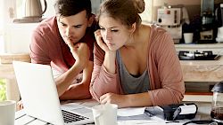 young couple staring at laptop surrounded by paperwork
