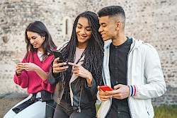 Female and male teenagers smiling and looking at their mobile phone screens