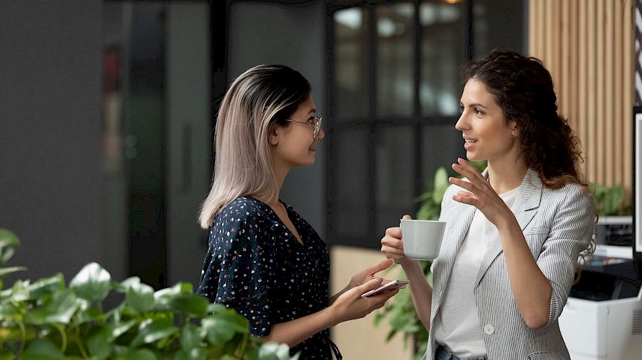 two female colleagues standing and talking with a coffee