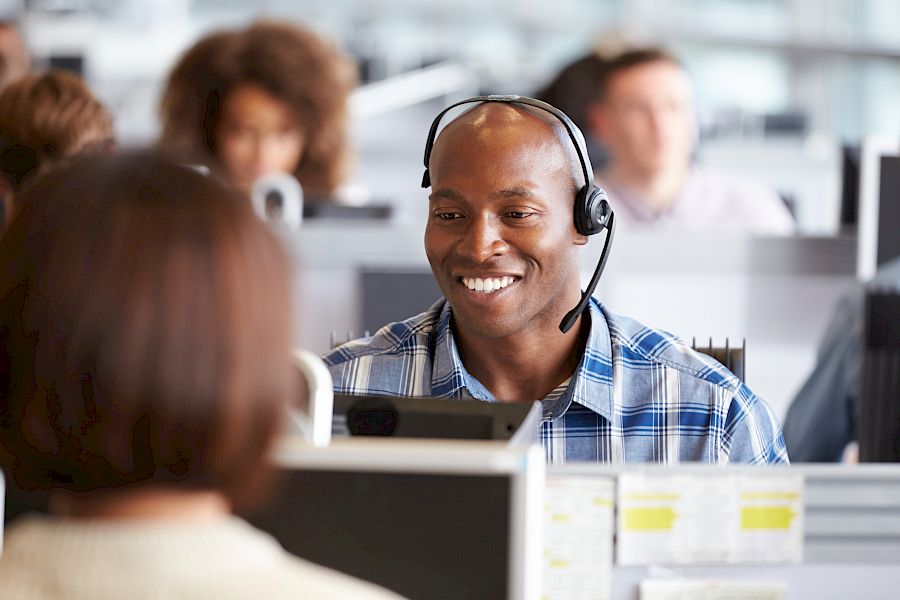 male customer services agent wearing a headset smiling in from of laptop