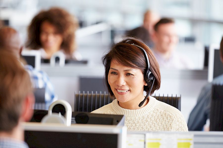 female customer services agent wearing a headset smiling in from of laptop