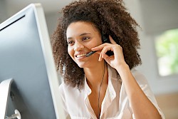 female customer service agent smiling wearing headset looking at laptop