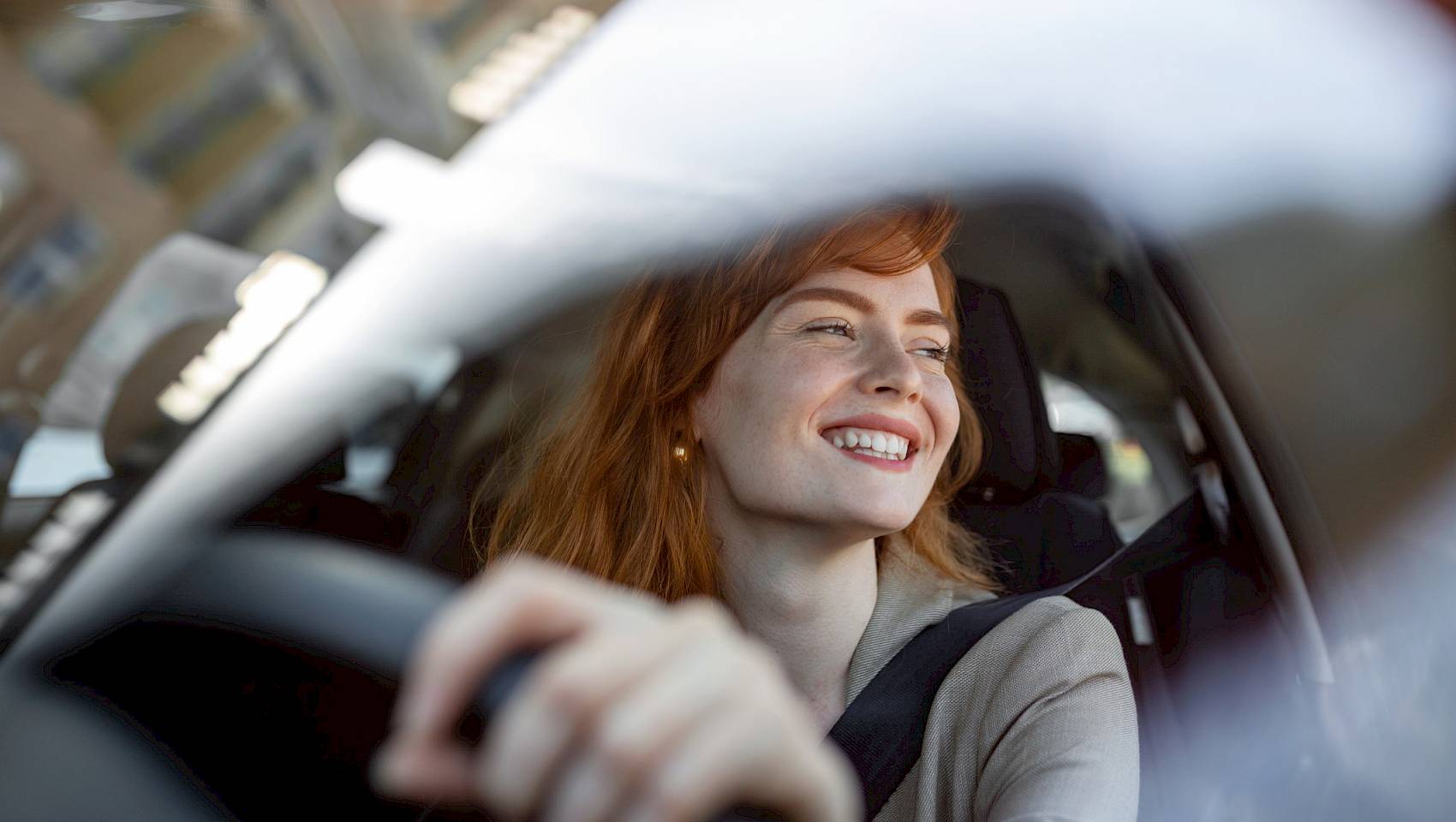 Red headed female smiling and driving a car