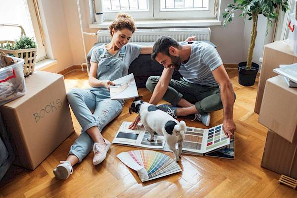 Young couple and dog sitting on floor in new house surrounded by moving boxes