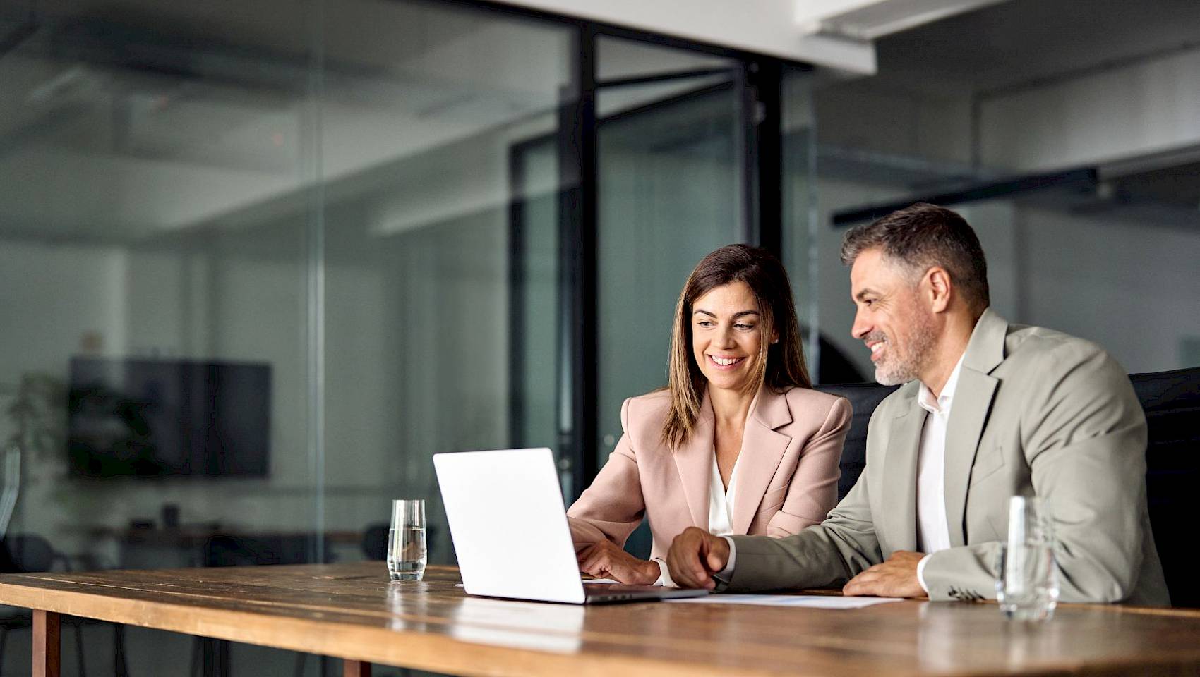 Female and male professional in office sharing laptop smiling