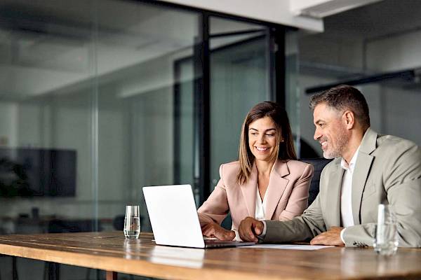 Female and male professional in office sharing laptop smiling