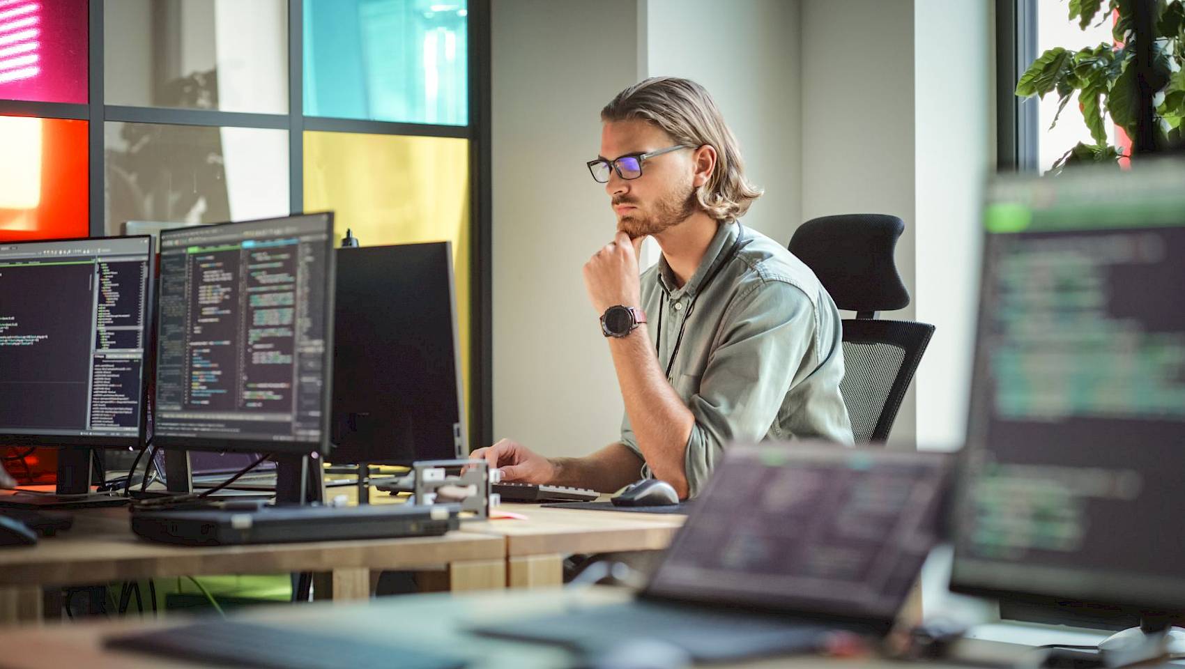 Male computer scientist wearing glasses looking at multiple computer screens with code on