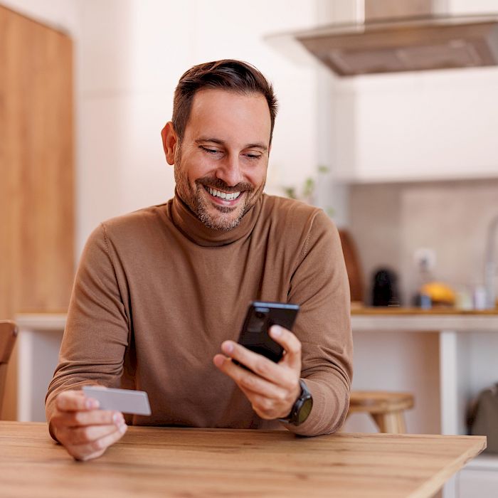 Young male smiling using mobile phone and making a payment using a bank card