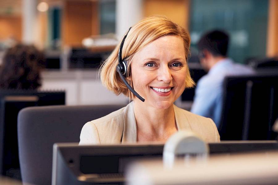 Professional woman wearing phone headset sat in fromt of a computer and smiling